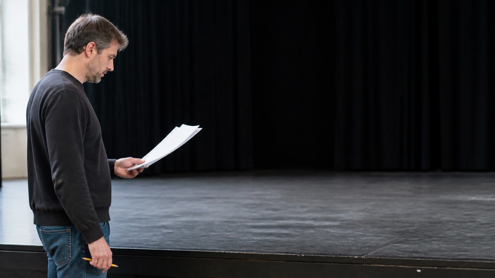 Writer reading pages beside an empty black-box stage